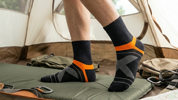 Person wearing black socks with orange accents standing inside a tent in a forest setting.