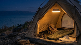 Camping tent with interior lighting by a body of water at night