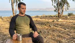 Man sitting outdoors by a lake holding a metal cup