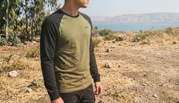 Person wearing a green and black long-sleeve shirt standing in a natural landscape with water in the background.