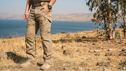 Person wearing beige pants standing in a dry landscape with a body of water and trees in the background