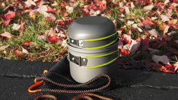 Metal container with green straps on a black mat with autumn leaves in the background