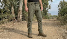 Person wearing green pants standing on a dirt path with trees in the background